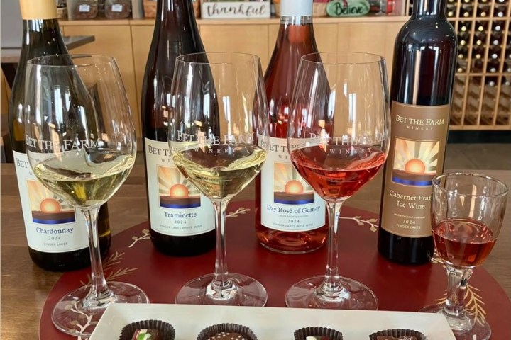 Four wine bottles with glasses and a tray of chocolates on a table.