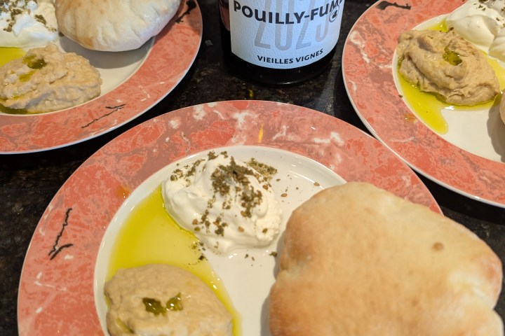 Plates with pita, hummus, and cream beside a bottle of Pouilly-Fumé wine.