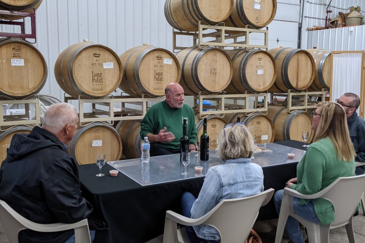 People sitting at a table in a winery with barrels stacked behind them.